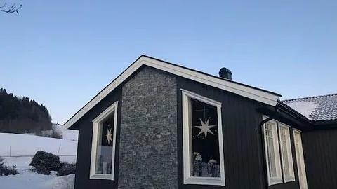 Nytt hus med mørk kledning og skifer ved inngangen, i vinterlys